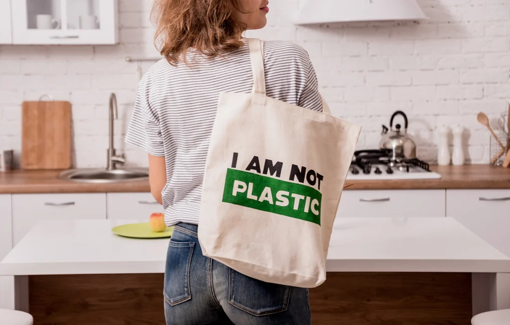 Donna con borsa in cotone riutilizzabile con scritta I am not plastic in una cucina minimal, simbolo dello stile di vita zero waste