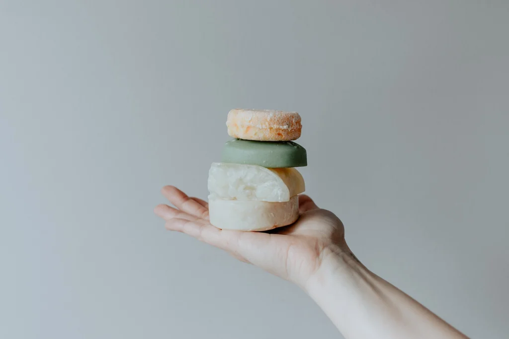 Shampoo e saponi solidi sostenibili impilati su una mano, ideali per una routine zero waste