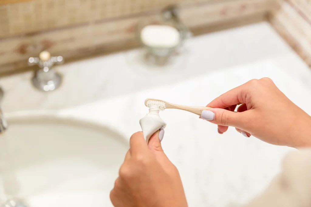 Persona che applica un dentifricio vegano e cruelty free su uno spazzolino ecologico in bambù