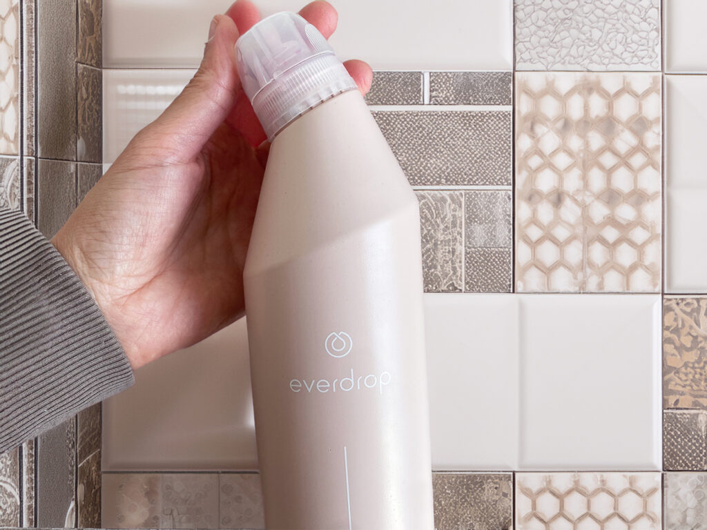 Pulizie di casa zero waste: Disincrostante per WC e sanitari Everdrop tenuto in mano davanti a piastrelle bagno