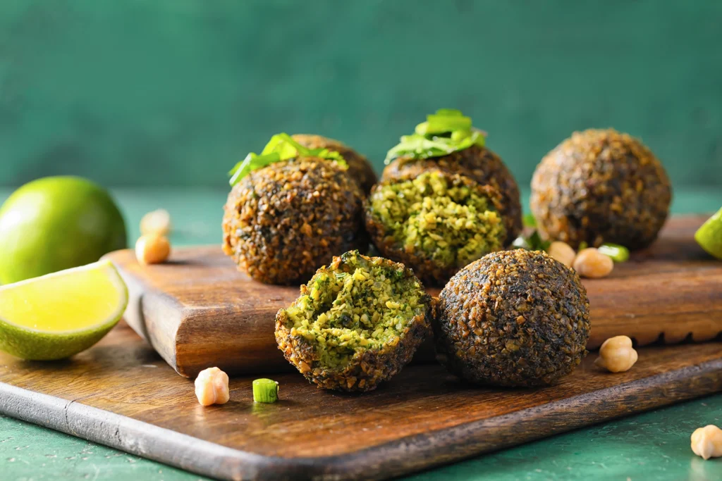 Falafel vegani croccanti serviti su un tagliere di legno con lime, ceci e prezzemolo
