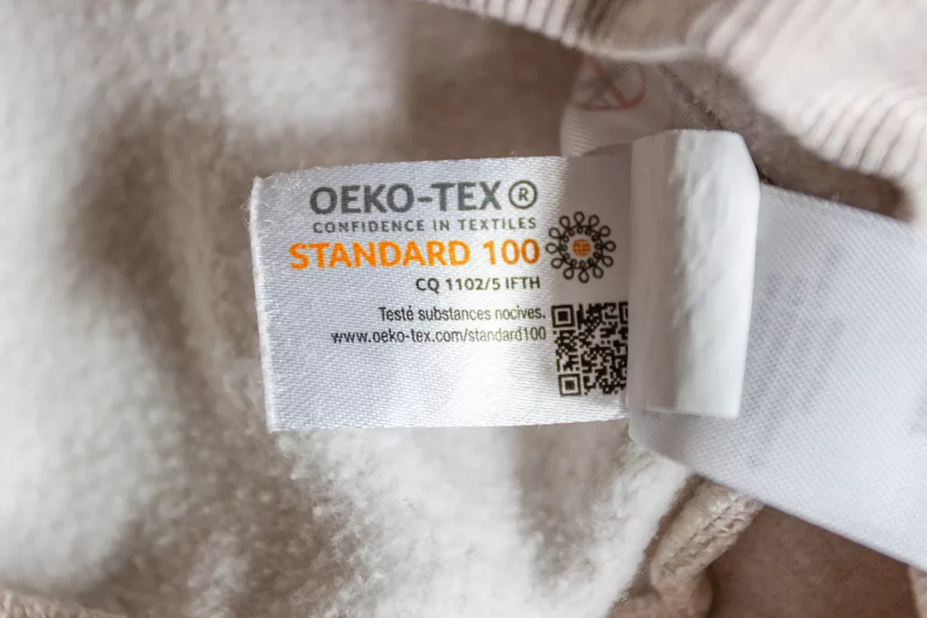 Etichetta OEKO-TEX® Standard 100 su un capo d’abbigliamento, garanzia di materiali sostenibili e materiali eco-friendly testati contro sostanze nocive. Certificazione per alternative sostenibili nella moda.