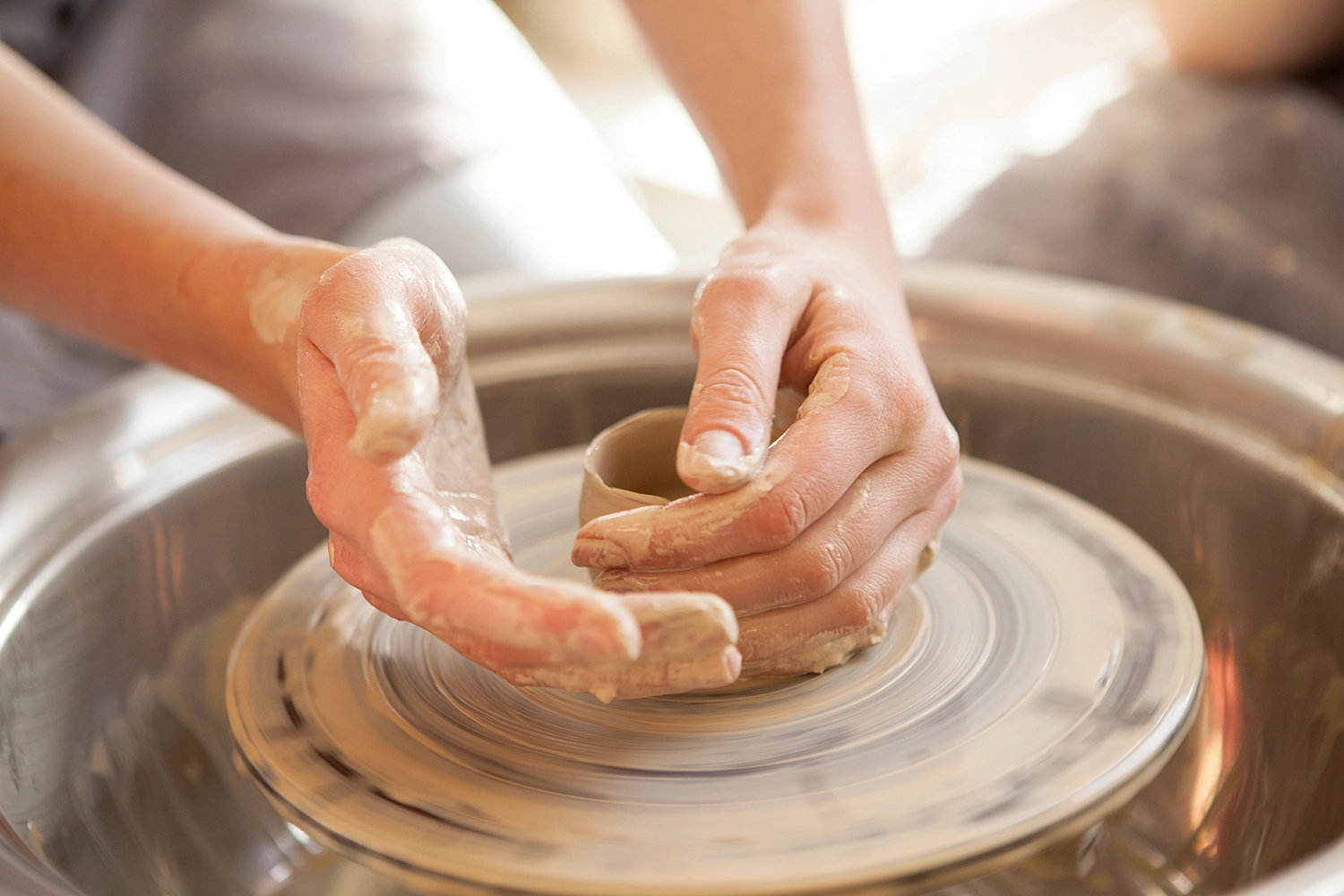 Mani di artigiane sostenibili che modellano l’argilla su un tornio, creando un vaso fatto a mano.