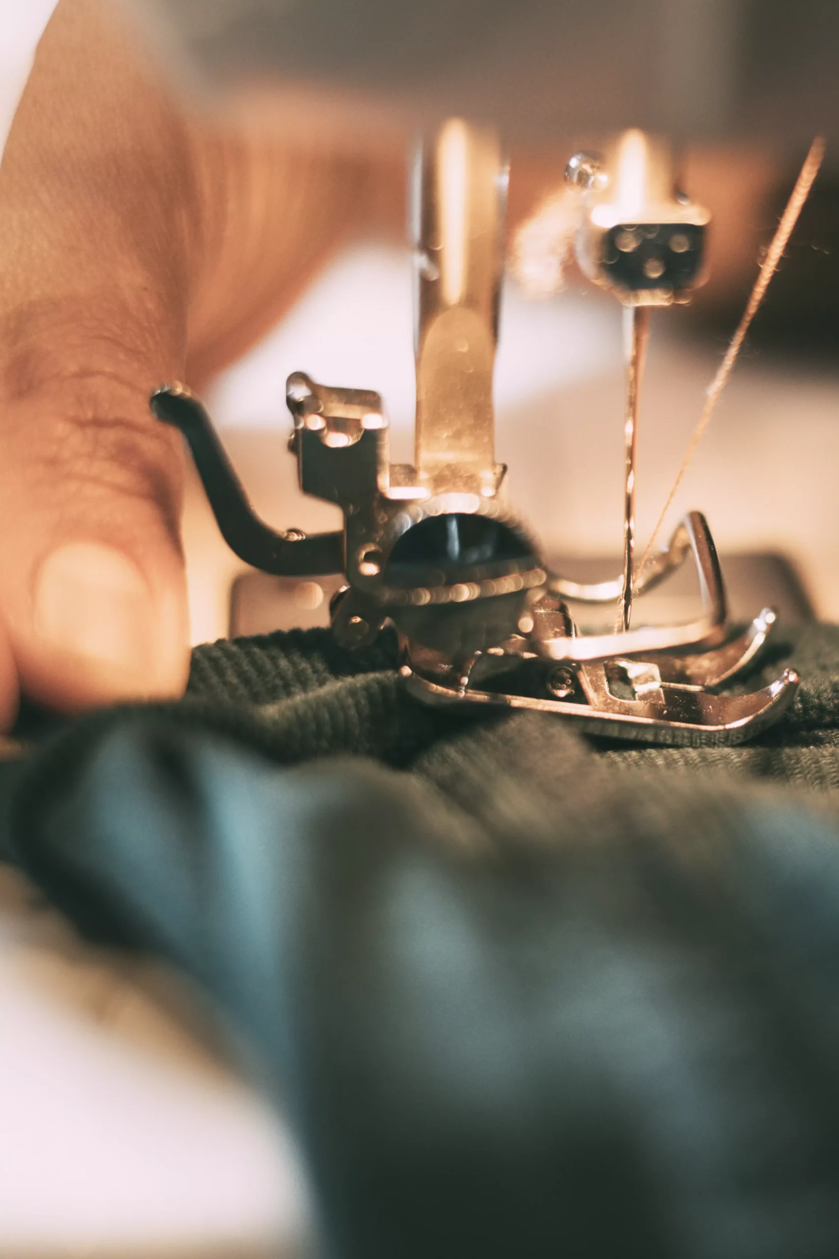 Mani di artigiane sostenibili mentre cuciono un tessuto con la macchina da cucire, in un processo di moda etica e consapevole.