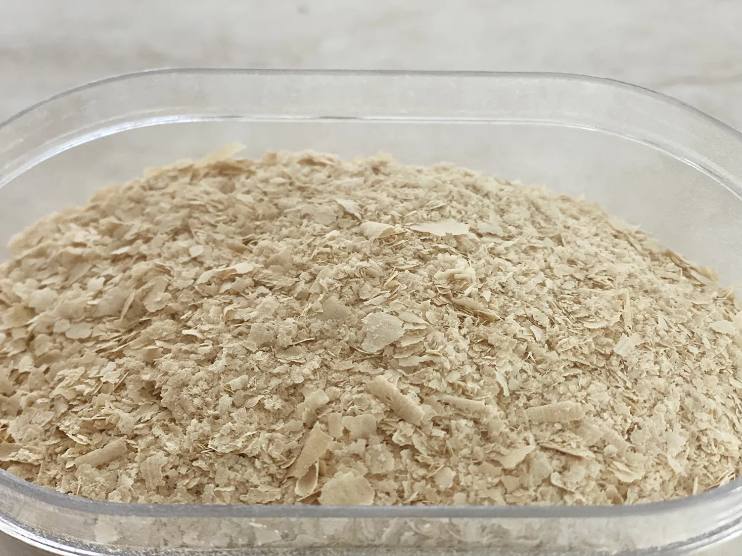 Dettaglio di lievito alimentare in fiocchi in un contenitore trasparente, ingrediente base nei prodotti vegan