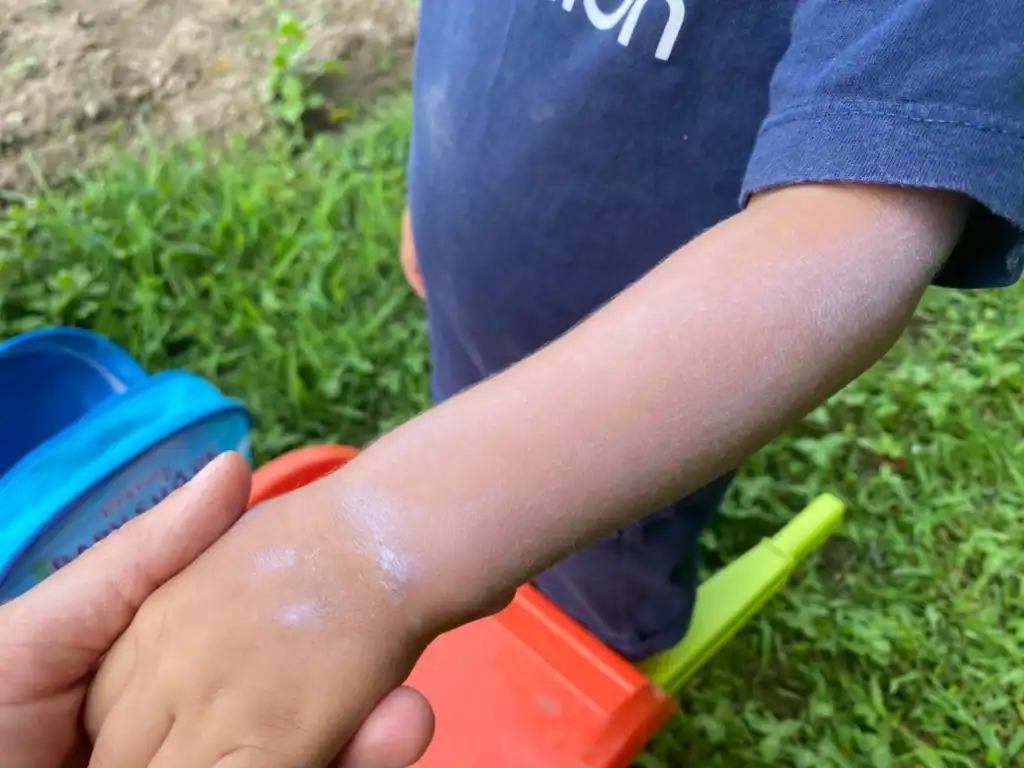 Applicazione crema solare Sole Bimbi Helan SPF50+ su pelle di bambino, effetto scudo bianco tipico dei filtri fisici, protezione alta per bambini.