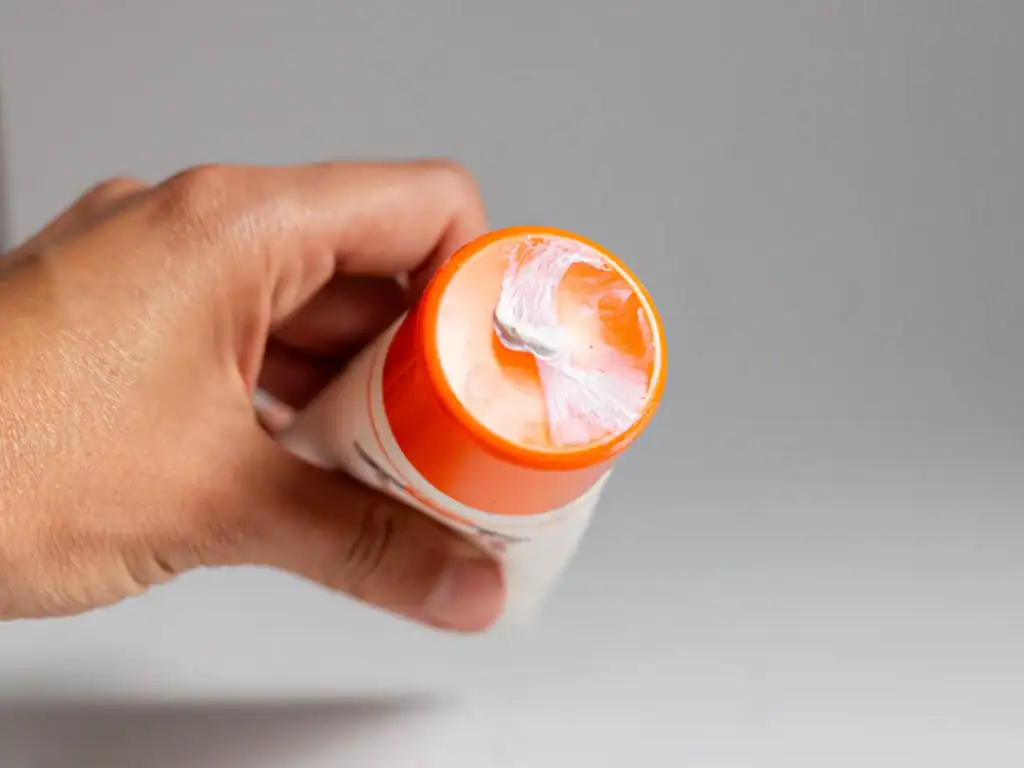 Dettaglio tappo crema solare Sole Bimbi Helan SPF50+, fuoriuscita di prodotto visibile, confezione arancione per la protezione solare dei bambini.