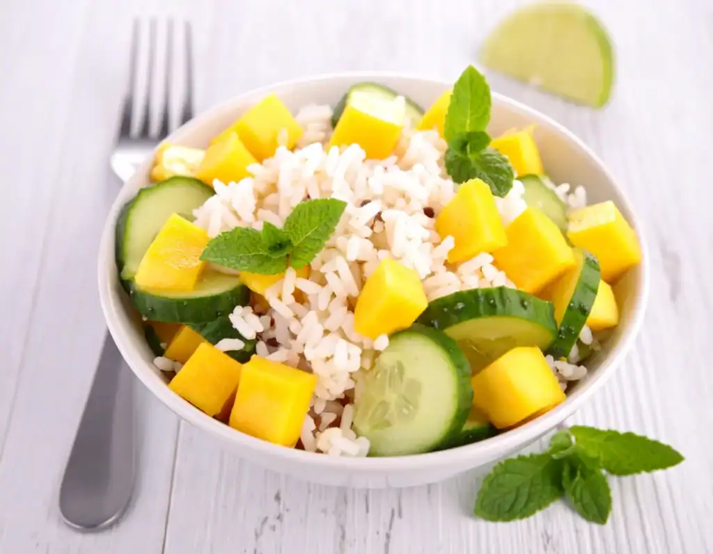 Ricette vegane estive: insalata di riso integrale con mango, cetriolo e menta fresca servita in una ciotola bianca