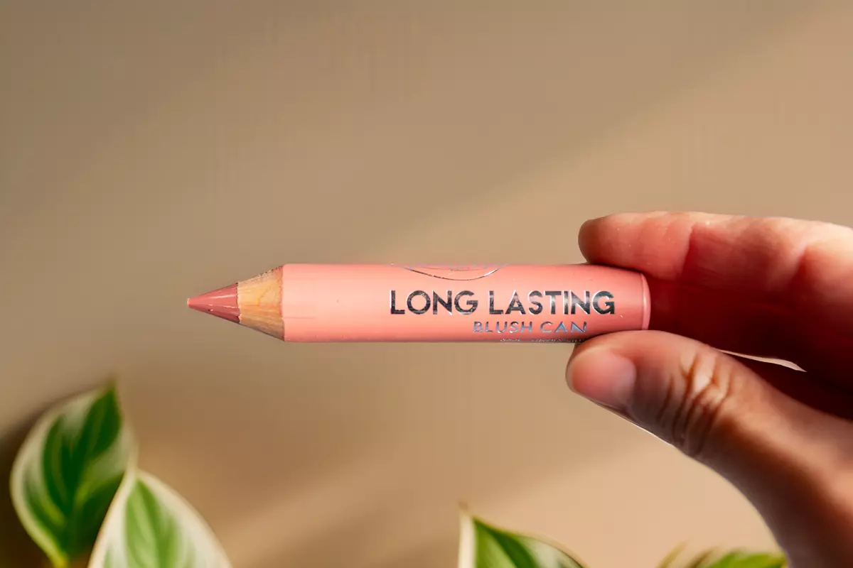 Blush Chubby puroBIO Long Lasting in tonalità pesca tenuto in mano su sfondo beige con foglie verdi