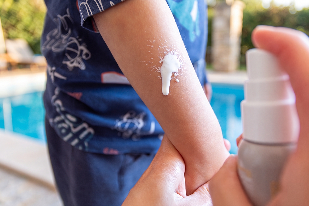 Applicazione della Crema Spray Solare SPF 50+ Baby di Bema sul braccio di un bambino a bordo piscina