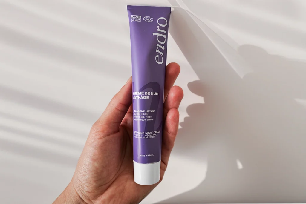 Crema notte anti age di Endro Cosmétiques tenuta in mano su sfondo chiaro con ombre naturali